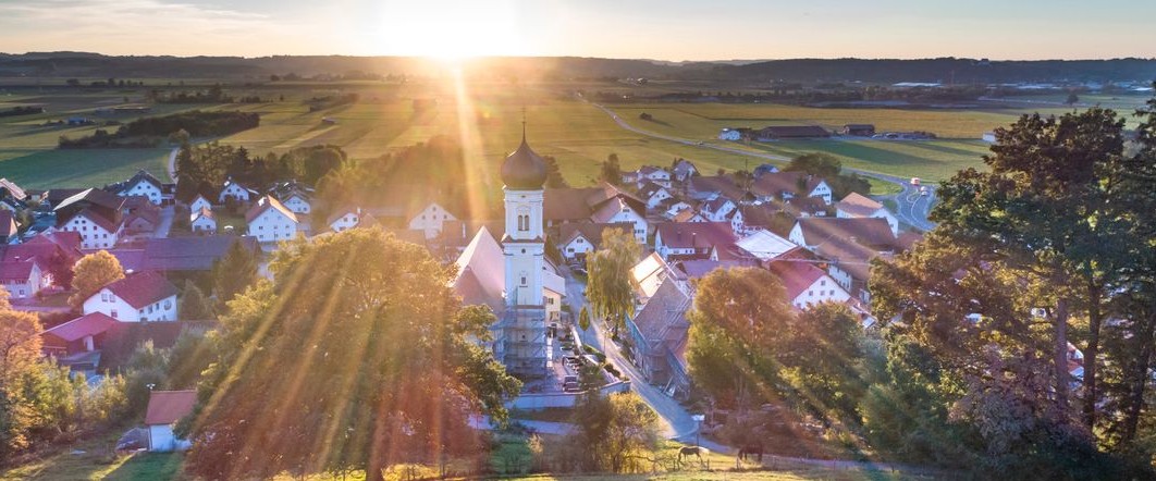 Blick über Bad Wörishofen im Sonnenaufgang, mit Kirchturm inmitten der Stadt